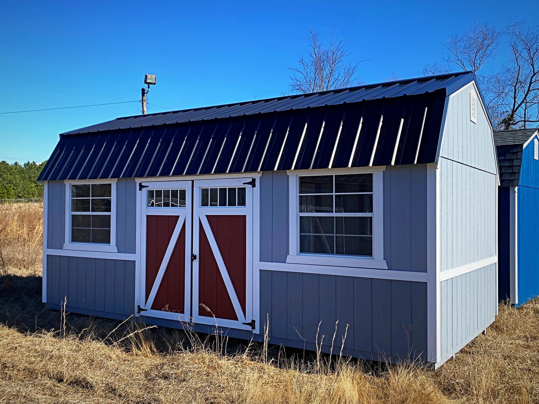 Lofted barn shed with a navy metal roof and red double barn doors on the Carolina Shed Depot lot